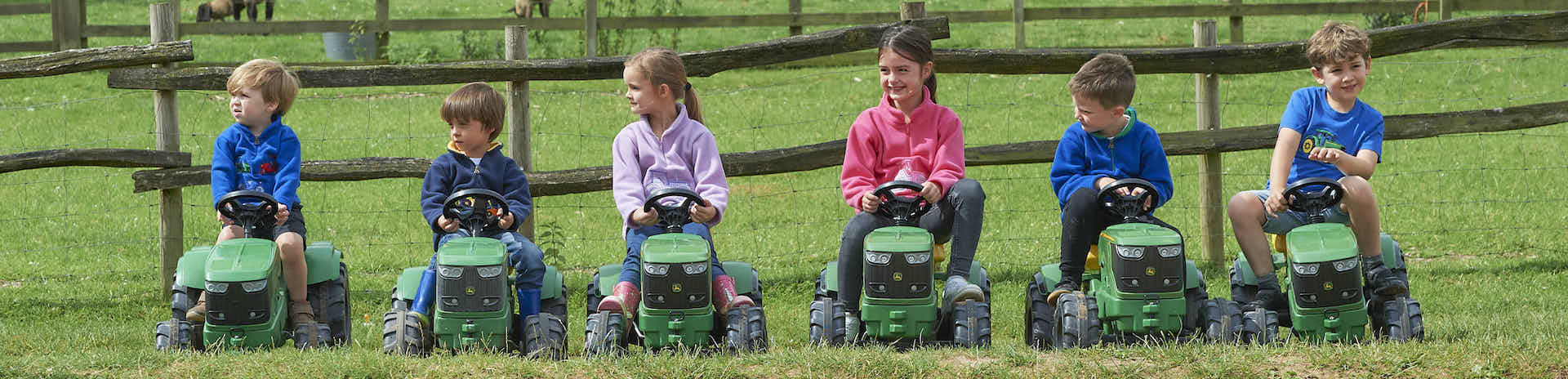 A group of children wearing ramblers clothing and riding toy tractors