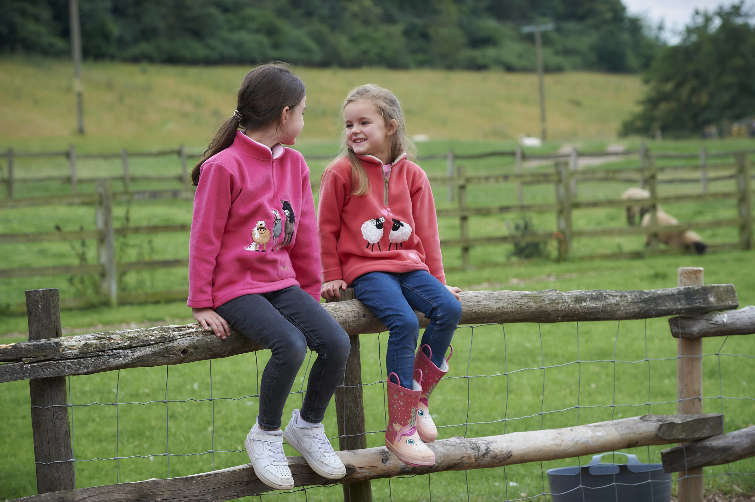 Children sitting on a fence wearing pink and red fleeces from ramblers clothing